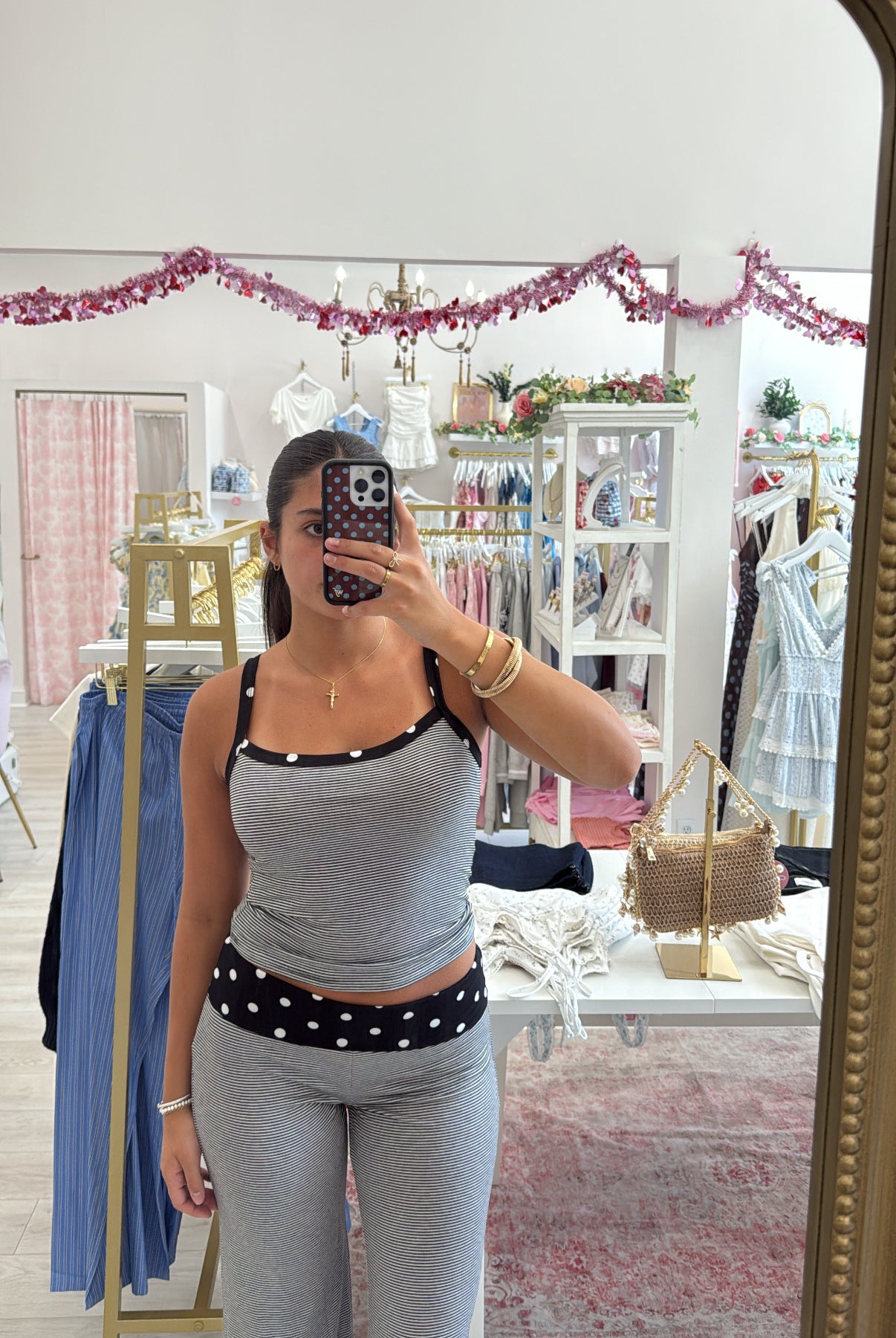 A woman takes a mirror selfie in a boutique wearing two-piece lounge set with a black and white polka dot waistband detail on the tank top and matching pants. cute loungewear matching set