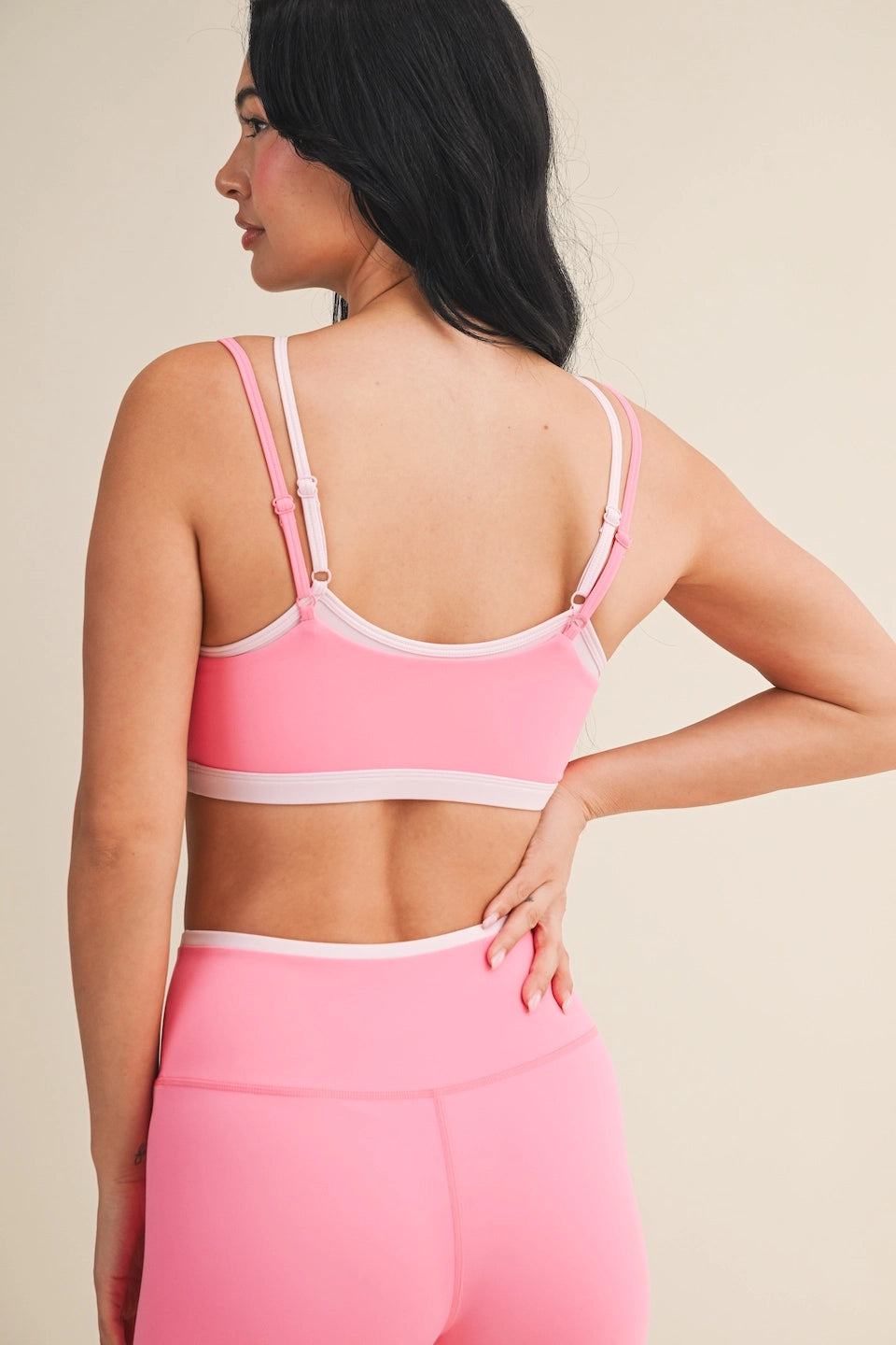 Woman wearing a double layered pink sports bra and leggings against a neutral background. cute athletic set