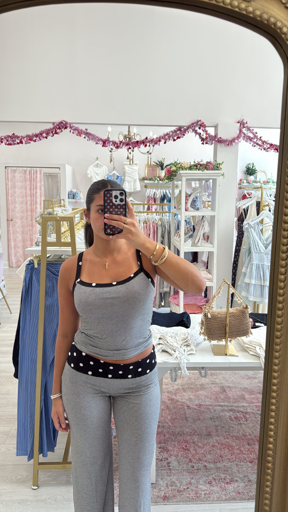 A woman takes a mirror selfie in a boutique wearing two-piece lounge set with a black and white polka dot waistband detail on the tank top and matching pants. cute loungewear matching set