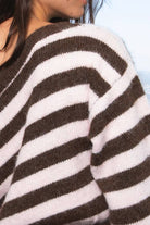 A close-up of a person wearing a fuzzy knit sweater with bold horizontal brown and off-white stripes.