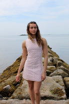 Woman wearing a white mini dress with red polka dots standing on rocks by the water. Fourth of July Mini Dress 