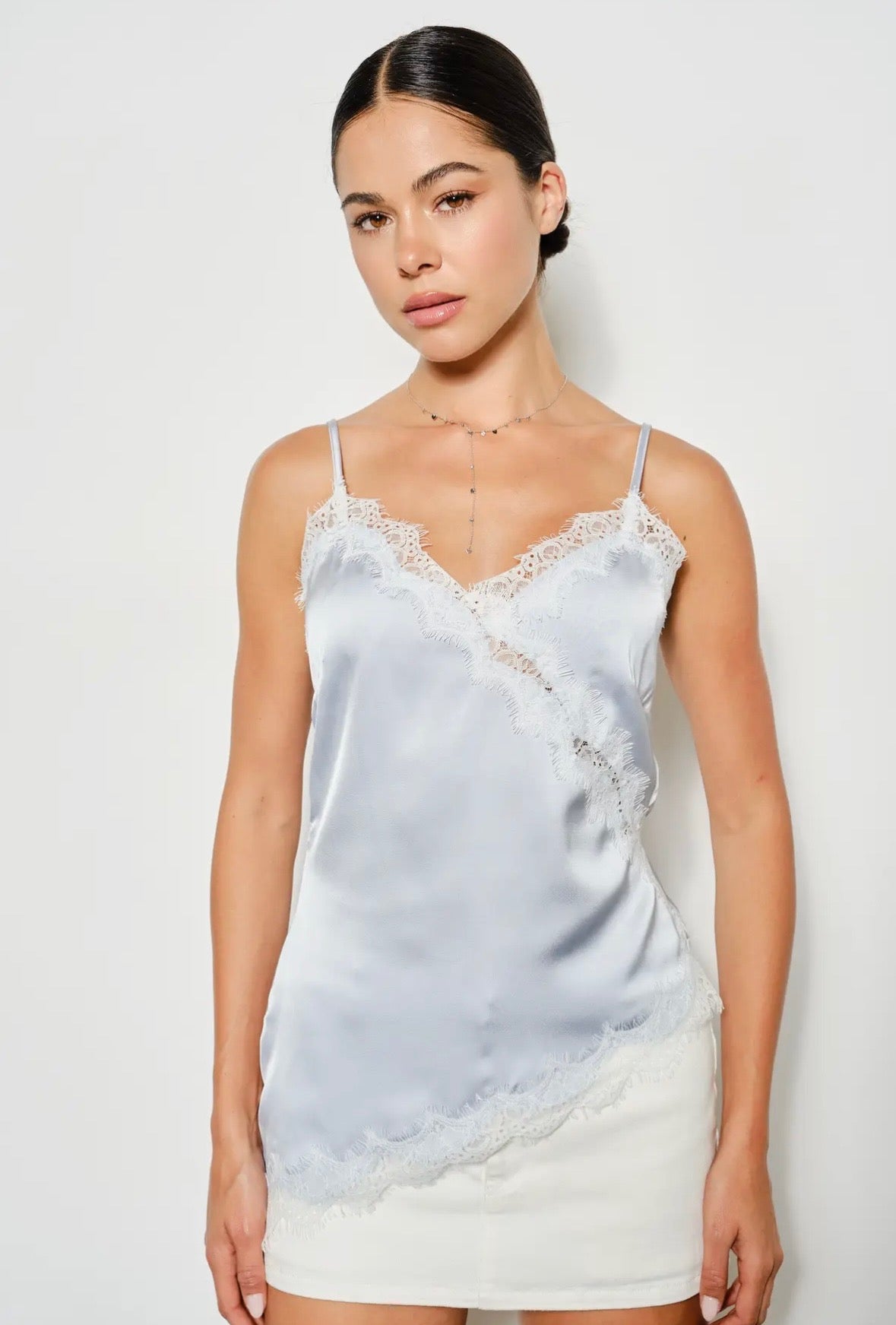 Woman wearing a light blue satin camisole with lace trim against a white background. Perfect going out top!