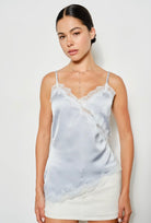 Woman wearing a light blue satin camisole with lace trim against a white background. Perfect going out top!