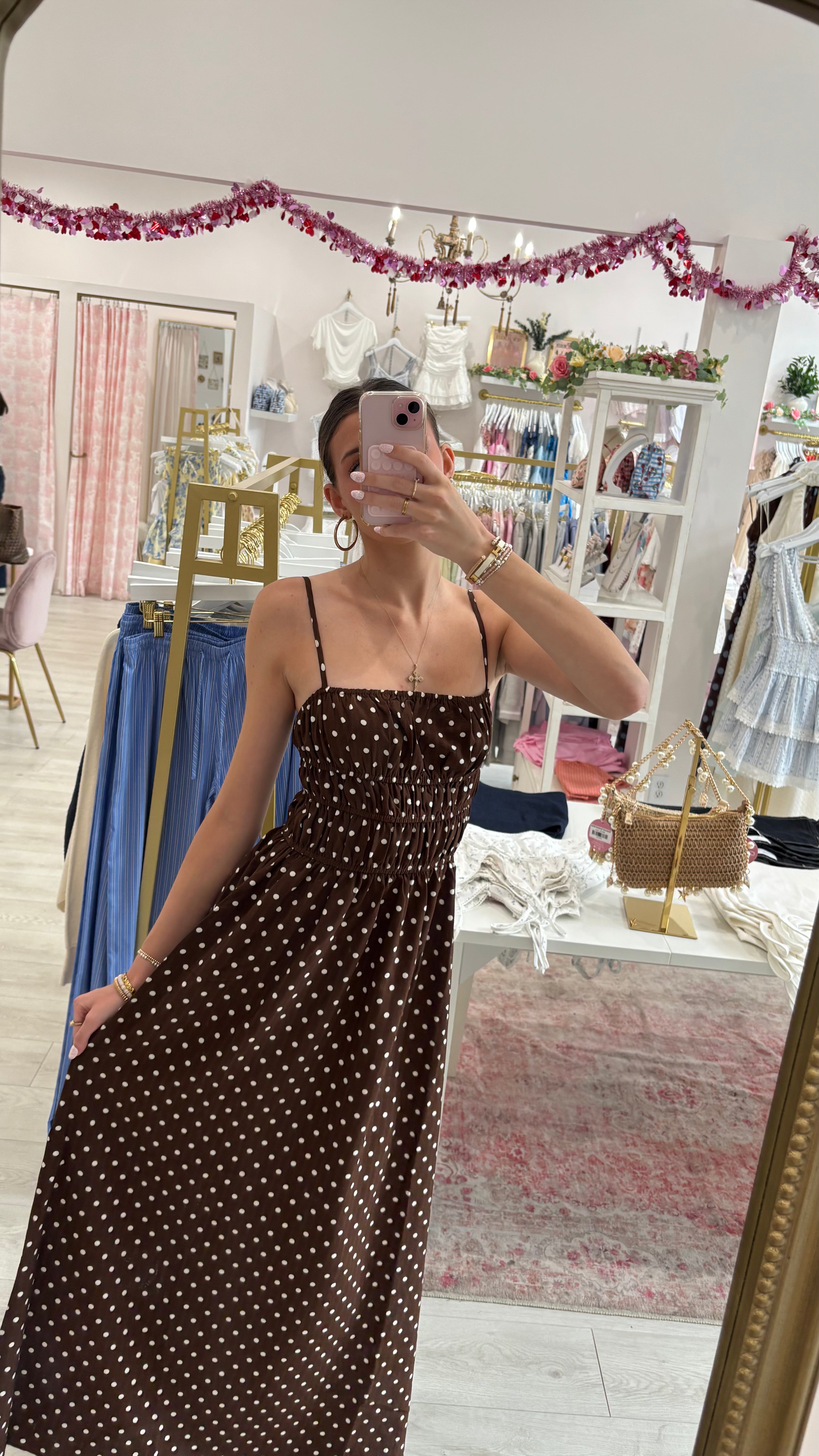Woman taking a mirror selfie wearing a brown polka dot dress in a store.